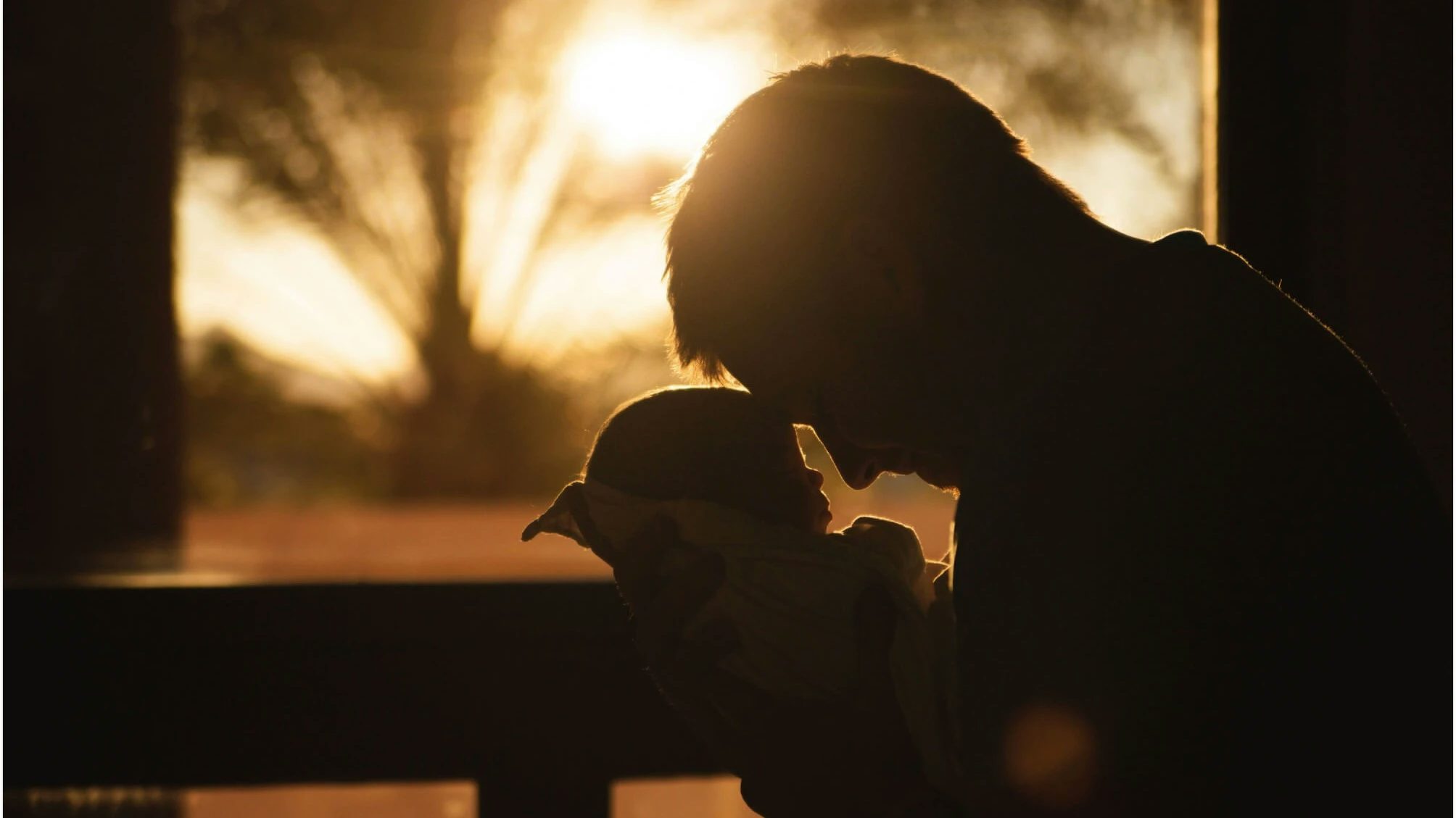 Dad holding baby forehead to forehead in backlight